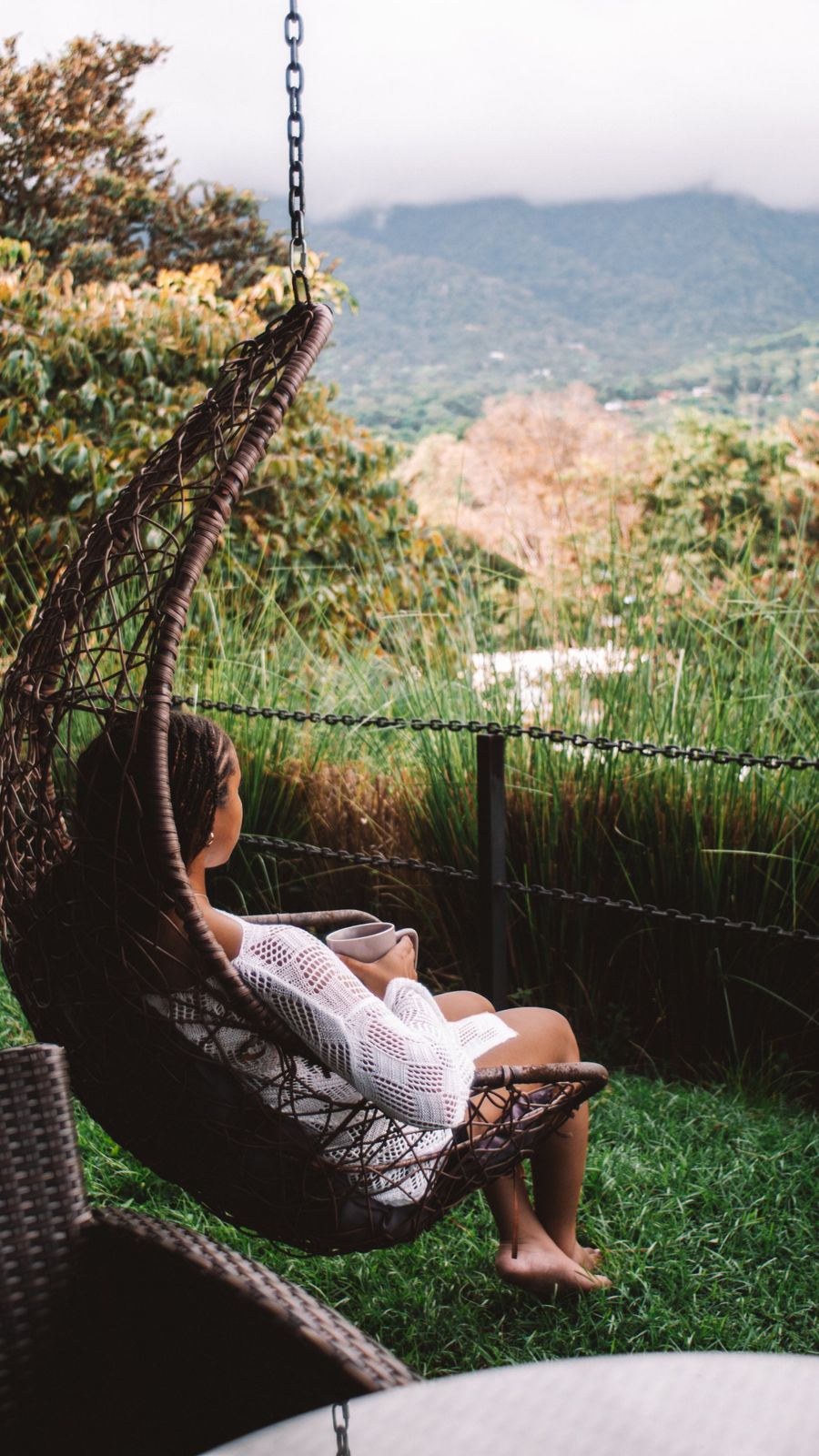 Guest relaxing in a hanging egg chair with coffee, overlooking the misty mountains