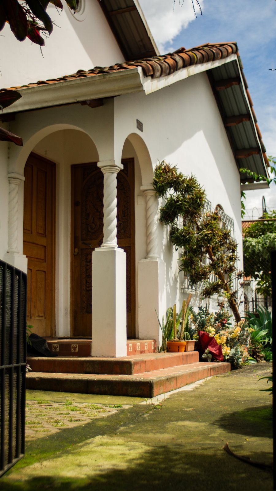 White colonial-style house with arched porch, carved wooden doors and succulents