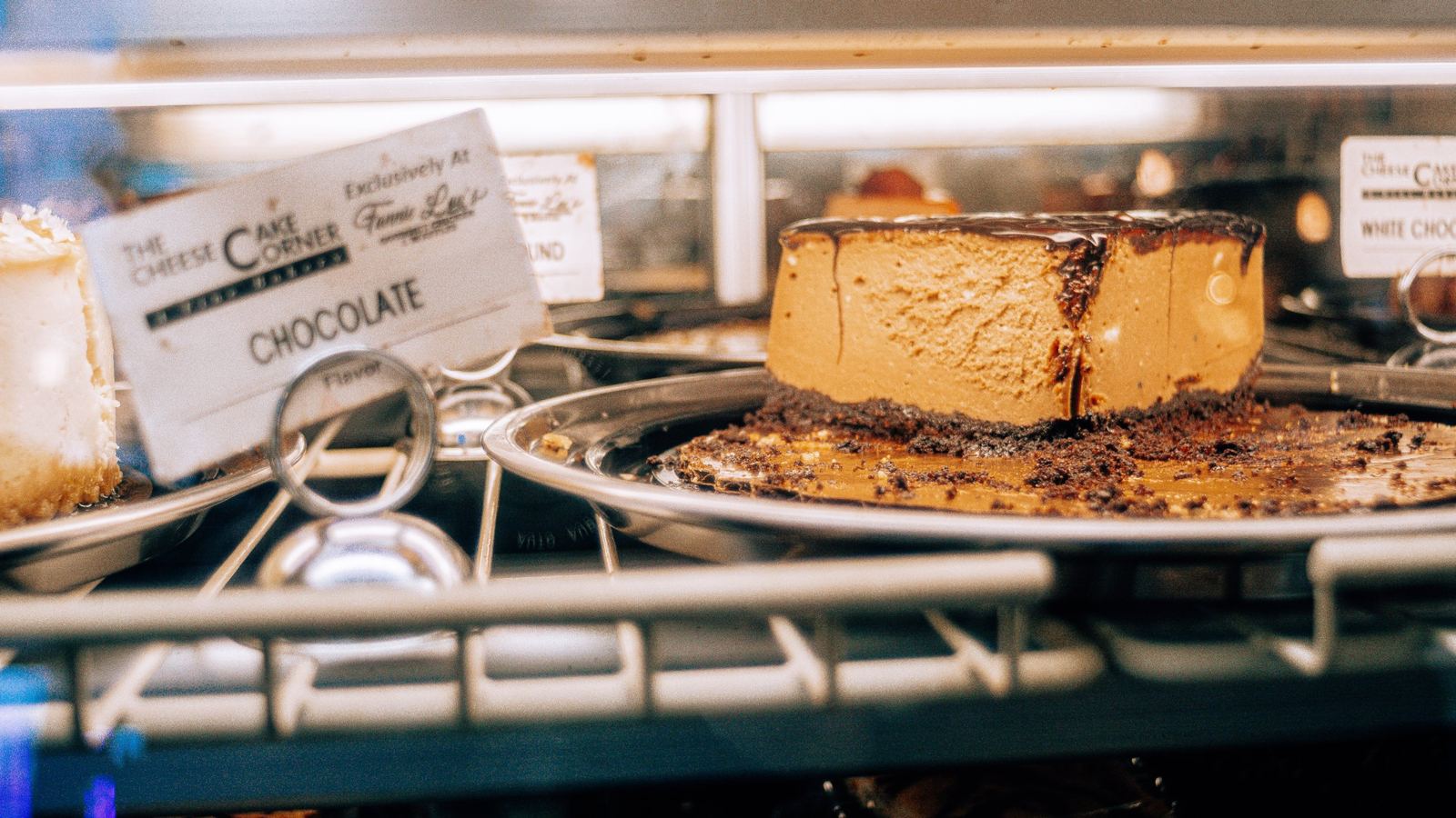 Chocolate cheesecake in the display case beside a Cheesecake Corner flavor card