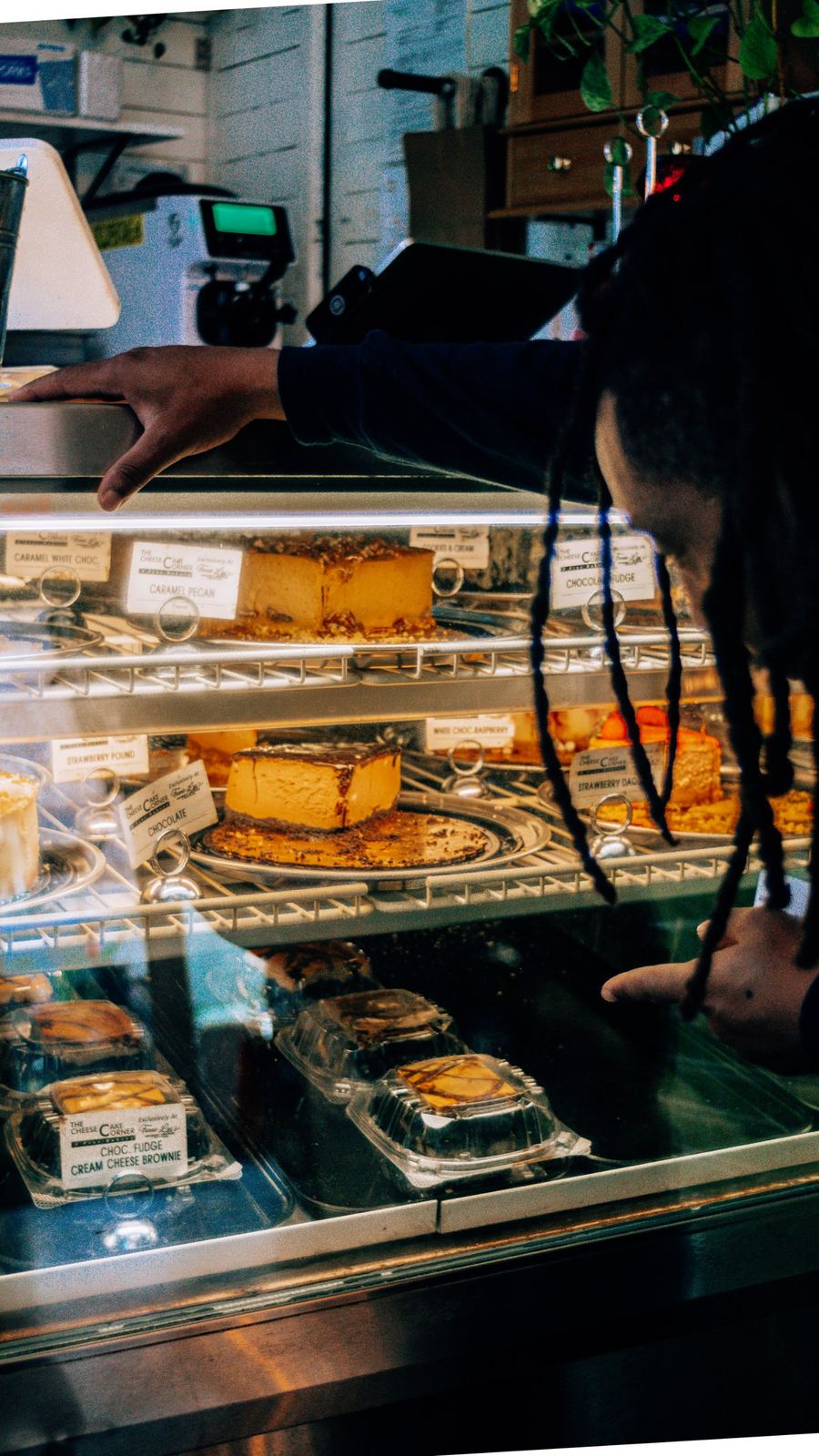 Guest leaning over the glass case to choose a cheesecake slice