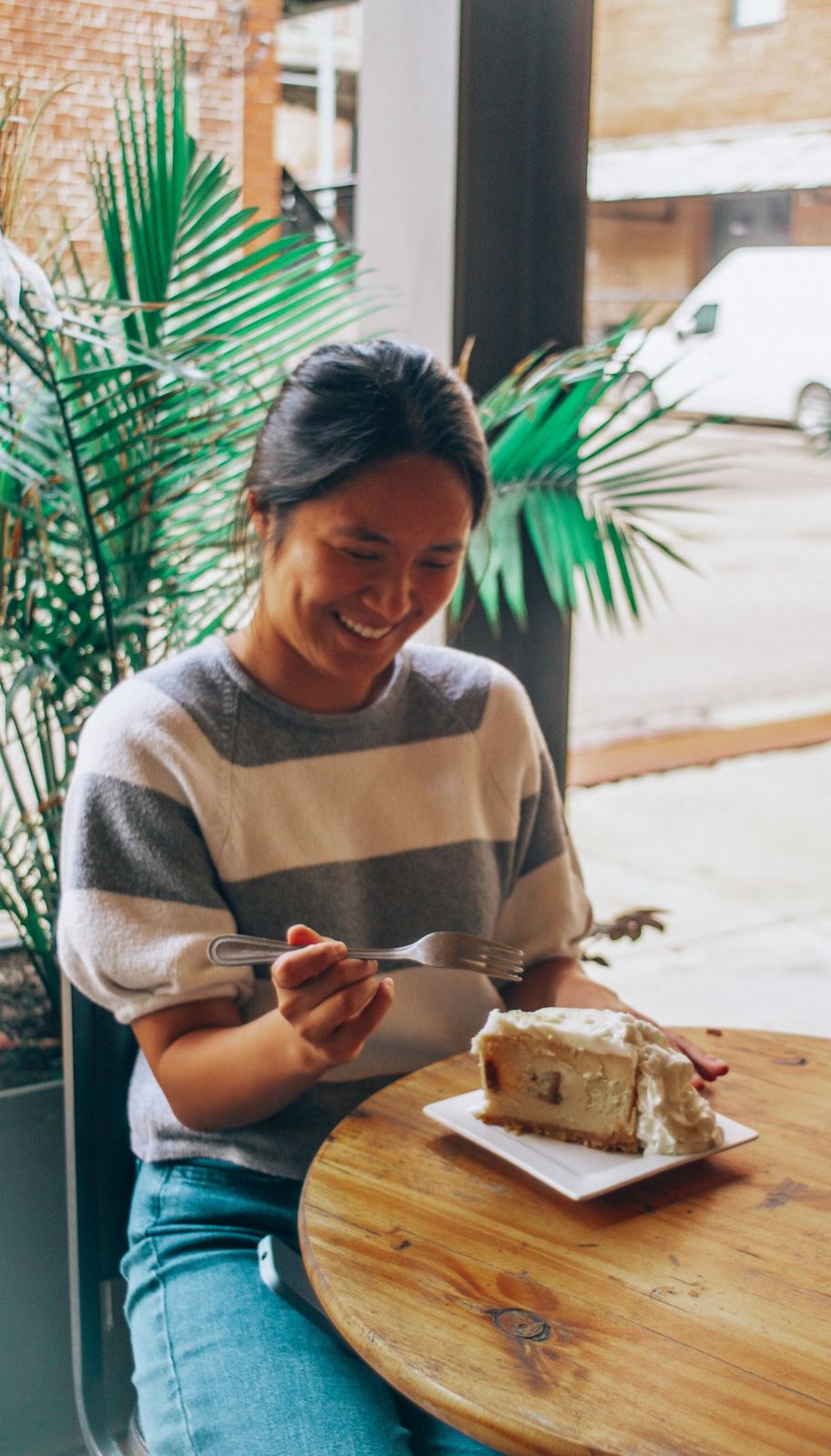 Guest smiling over a slice of cheesecake at a wooden cafe table