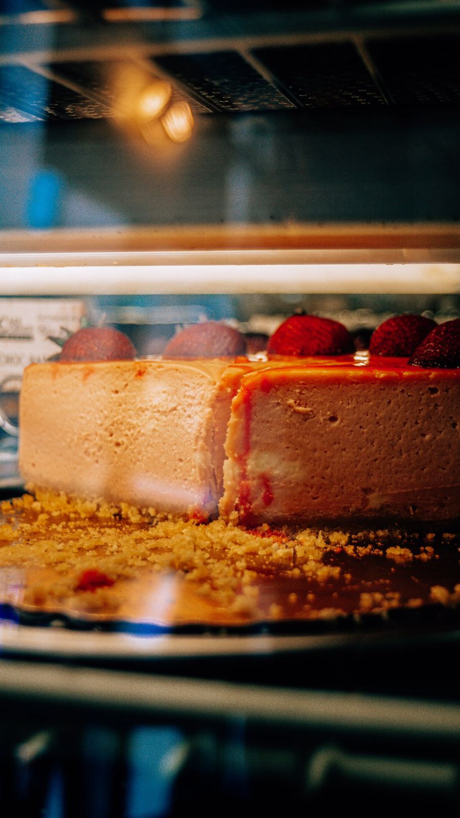 Strawberry cheesecake topped with glaze and berries behind the glass