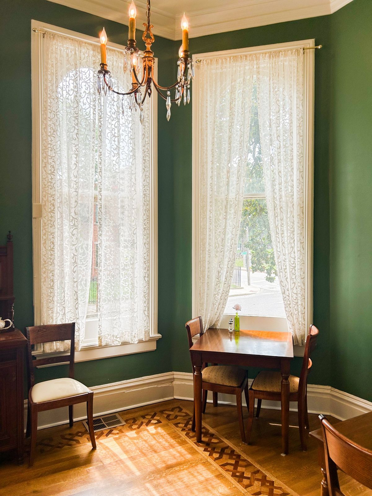 Green dining room with lace curtains, a crystal chandelier and a table for two