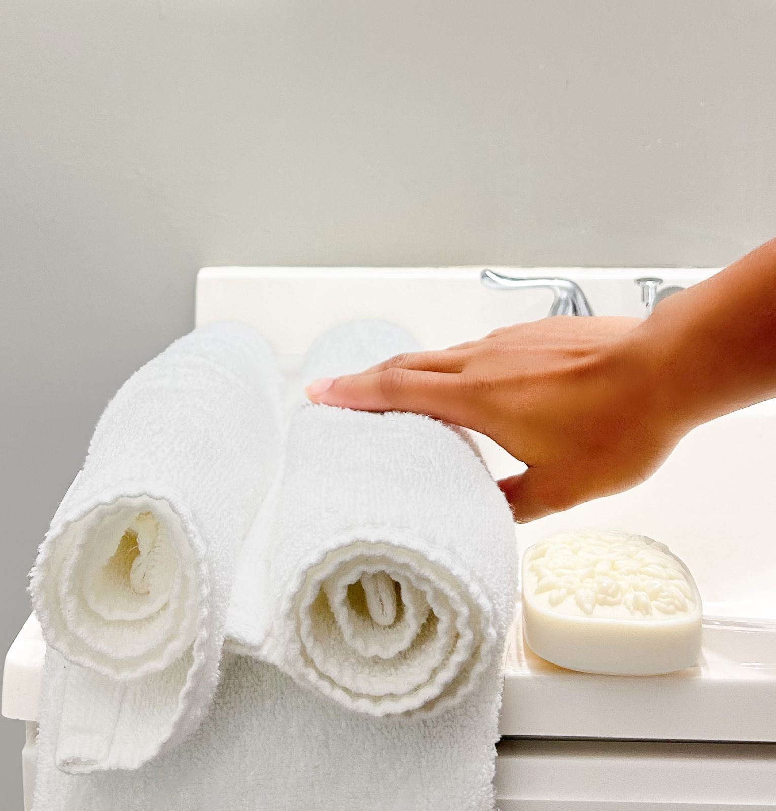 Hand resting on rolled white towels beside an embossed soap bar